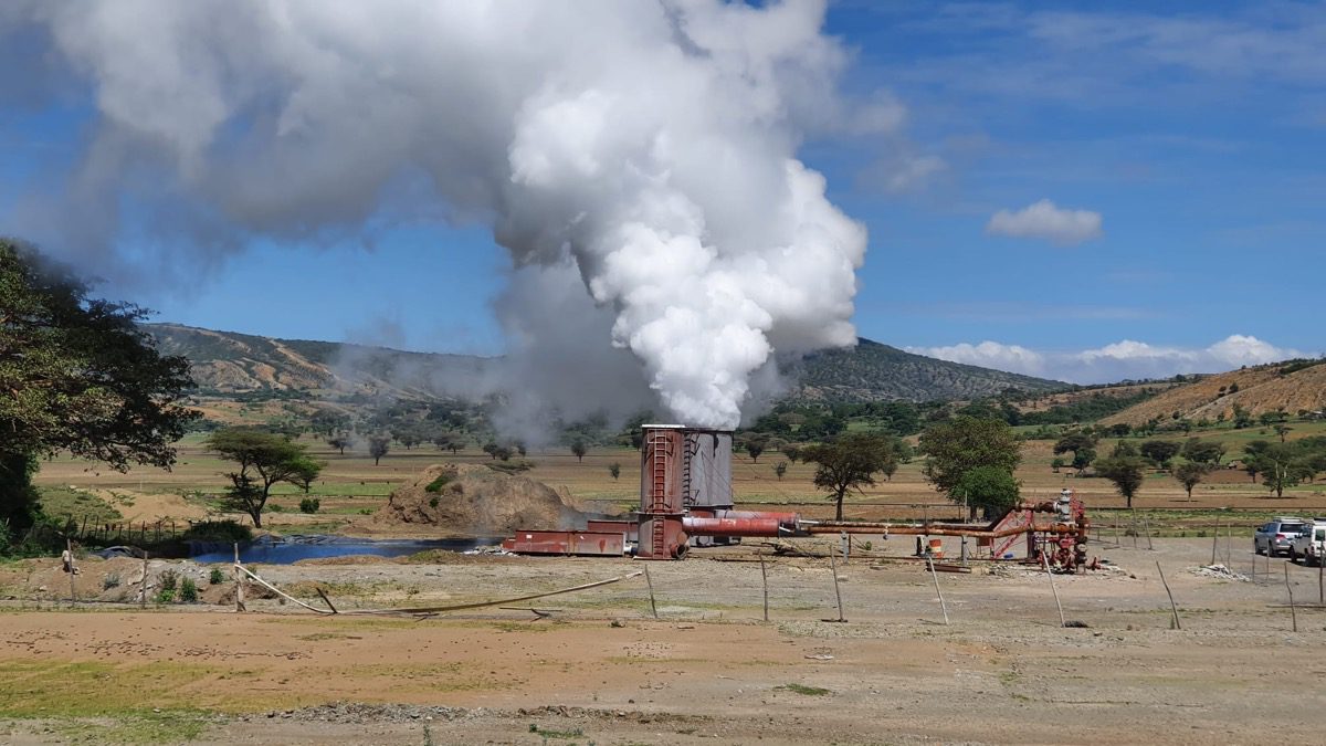 Geothermal drilling site with steam rising from a geothermal well, surrounded by an expansive, dry, and mountainous landscape.