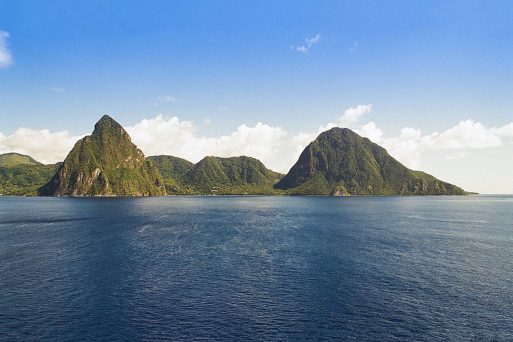 Tropical island landscape with steep green hills rising from the sea under a clear blue sky