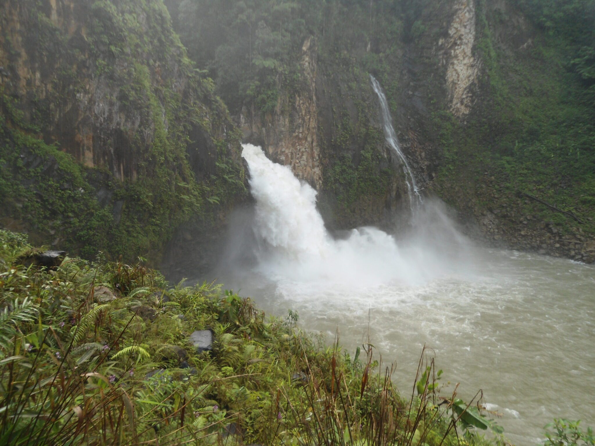 Powerful water outflow from a tunnel into a river surrounded by steep cliffs and dense green vegetation