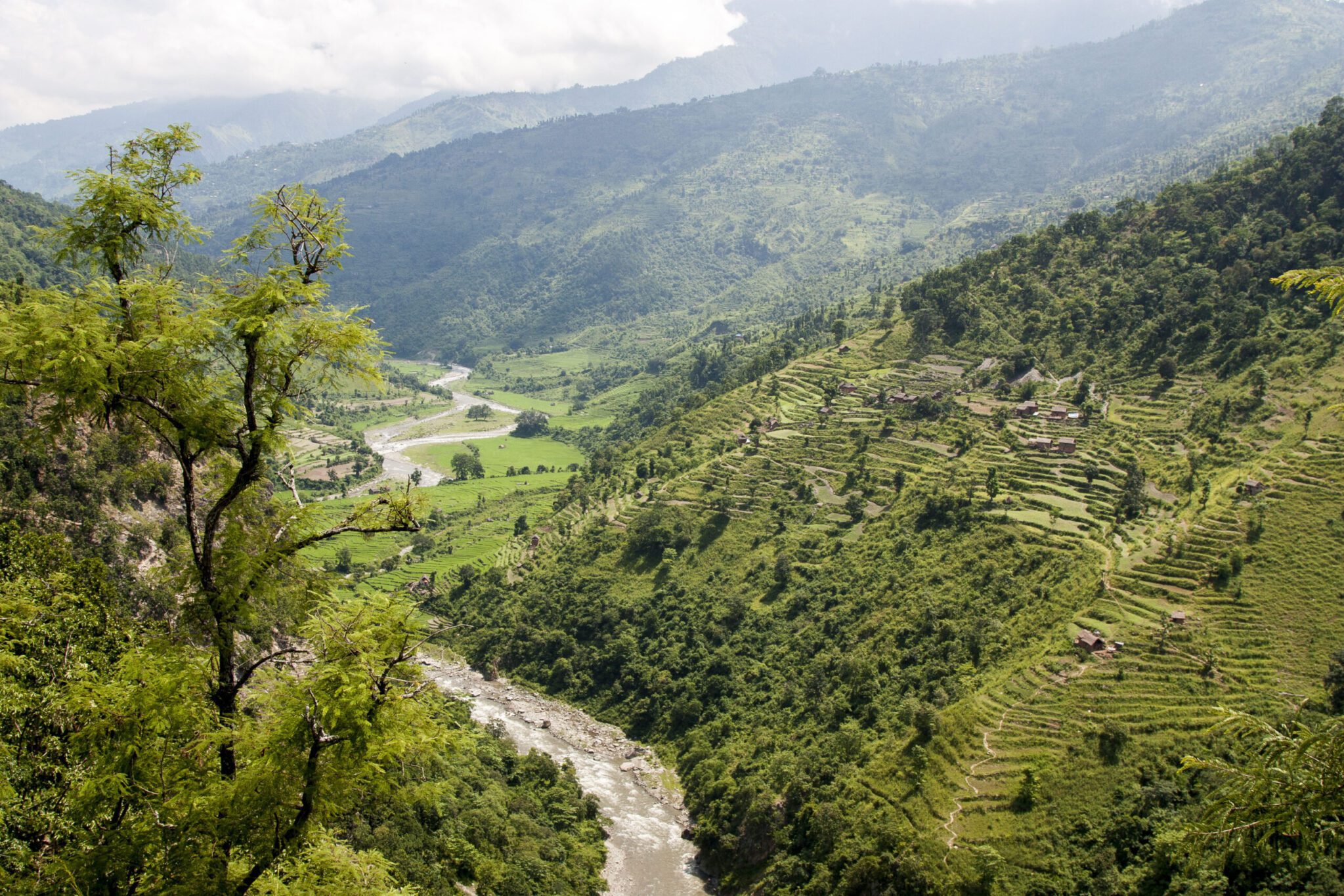 Scenic mountain valley with terraced fields, scattered houses, and a winding river flowing through lush green hills
