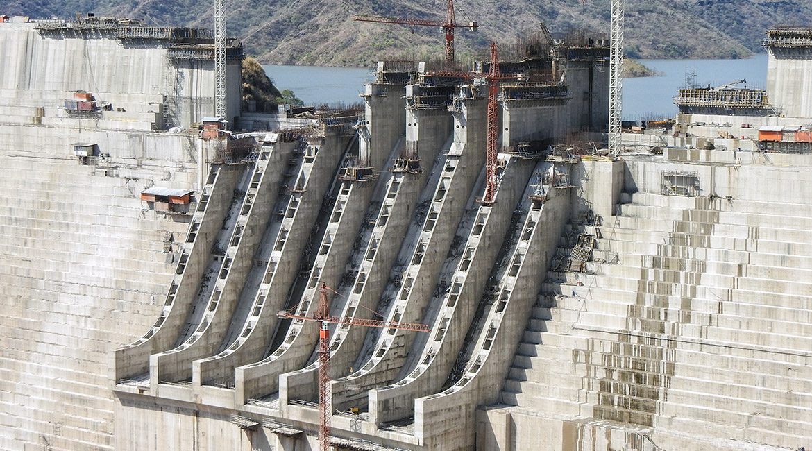 Close-up view of a large concrete dam under construction, with multiple spillways and cranes visible