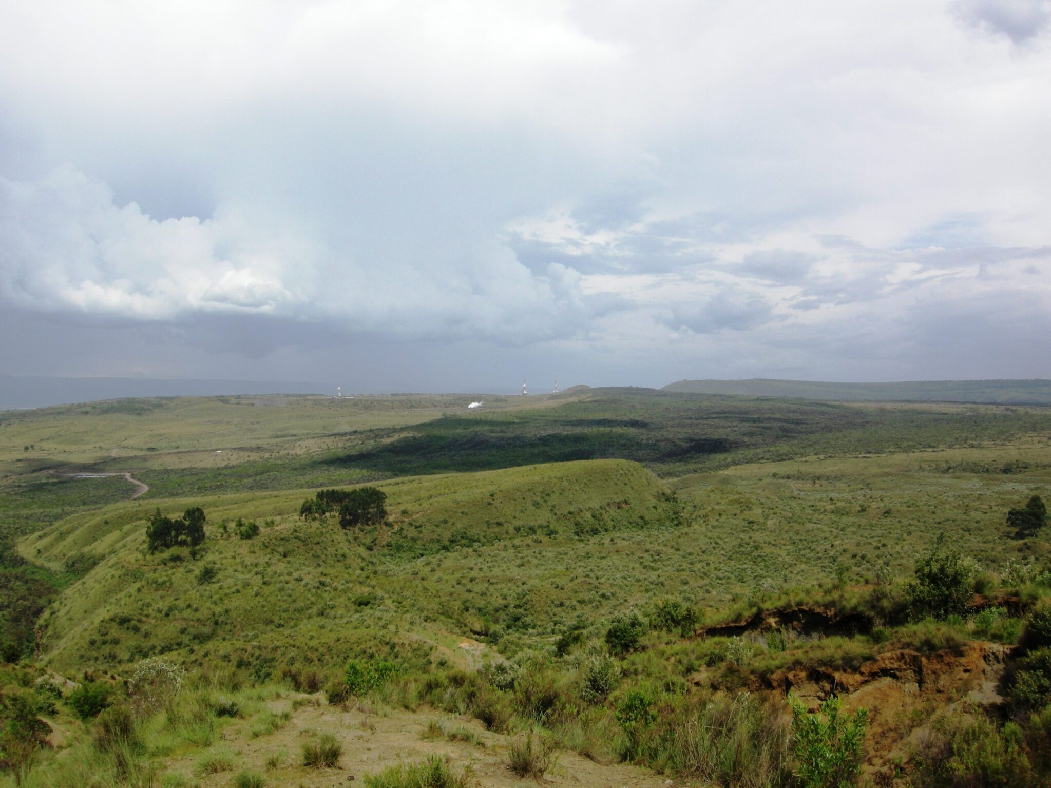 Wide view of a green, open plateau landscape under a cloudy sky, with rolling hills and sparse vegetation