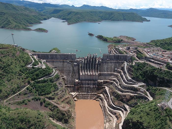 Aerial view of a large dam and reservoir set in a mountainous landscape, with terraced construction and surrounding infrastructure.