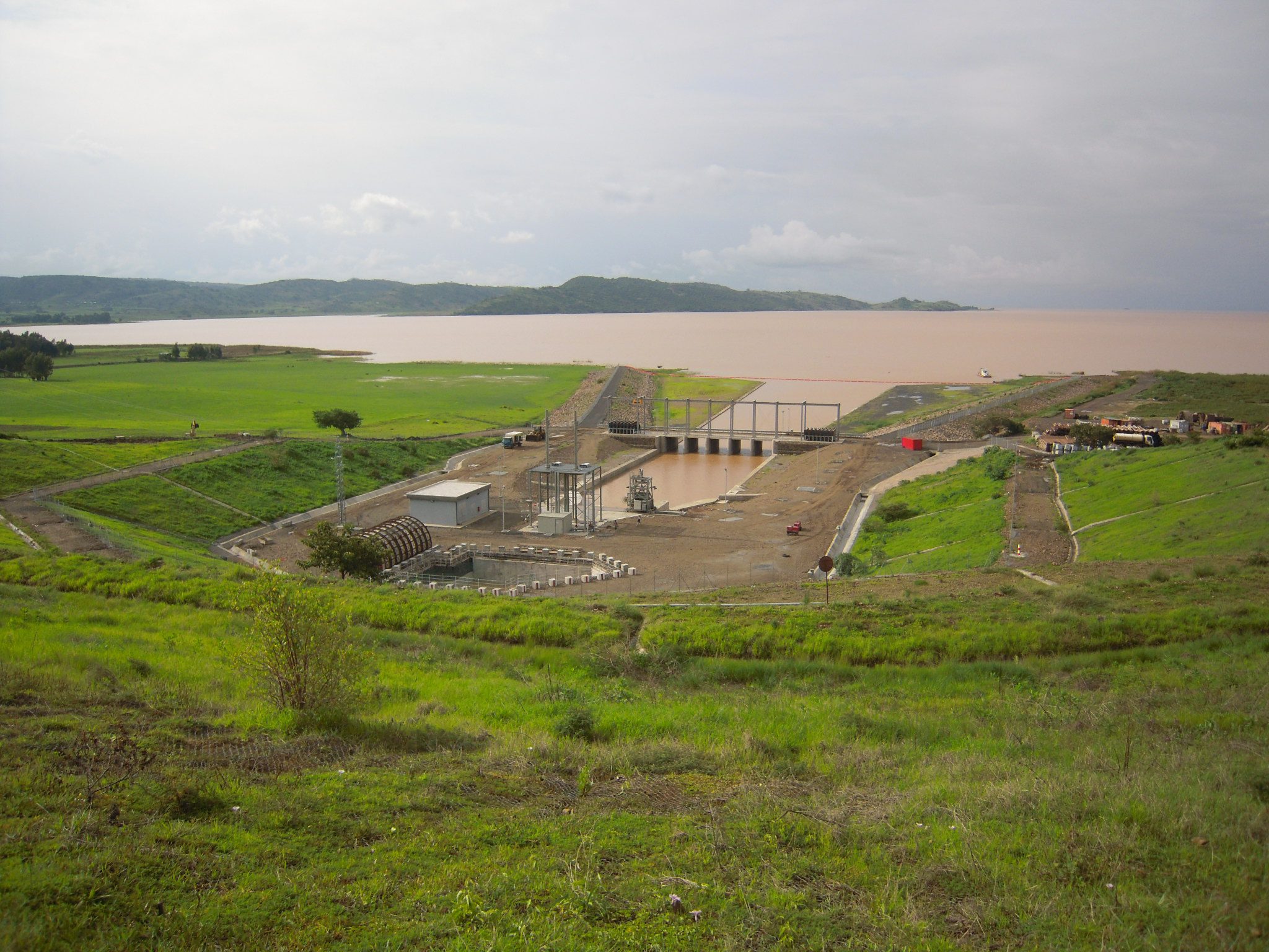Wide-angle view of a Hydropower Project intake and surface facilities, showing the reservoir and infrastructure in a green, hilly landscape.