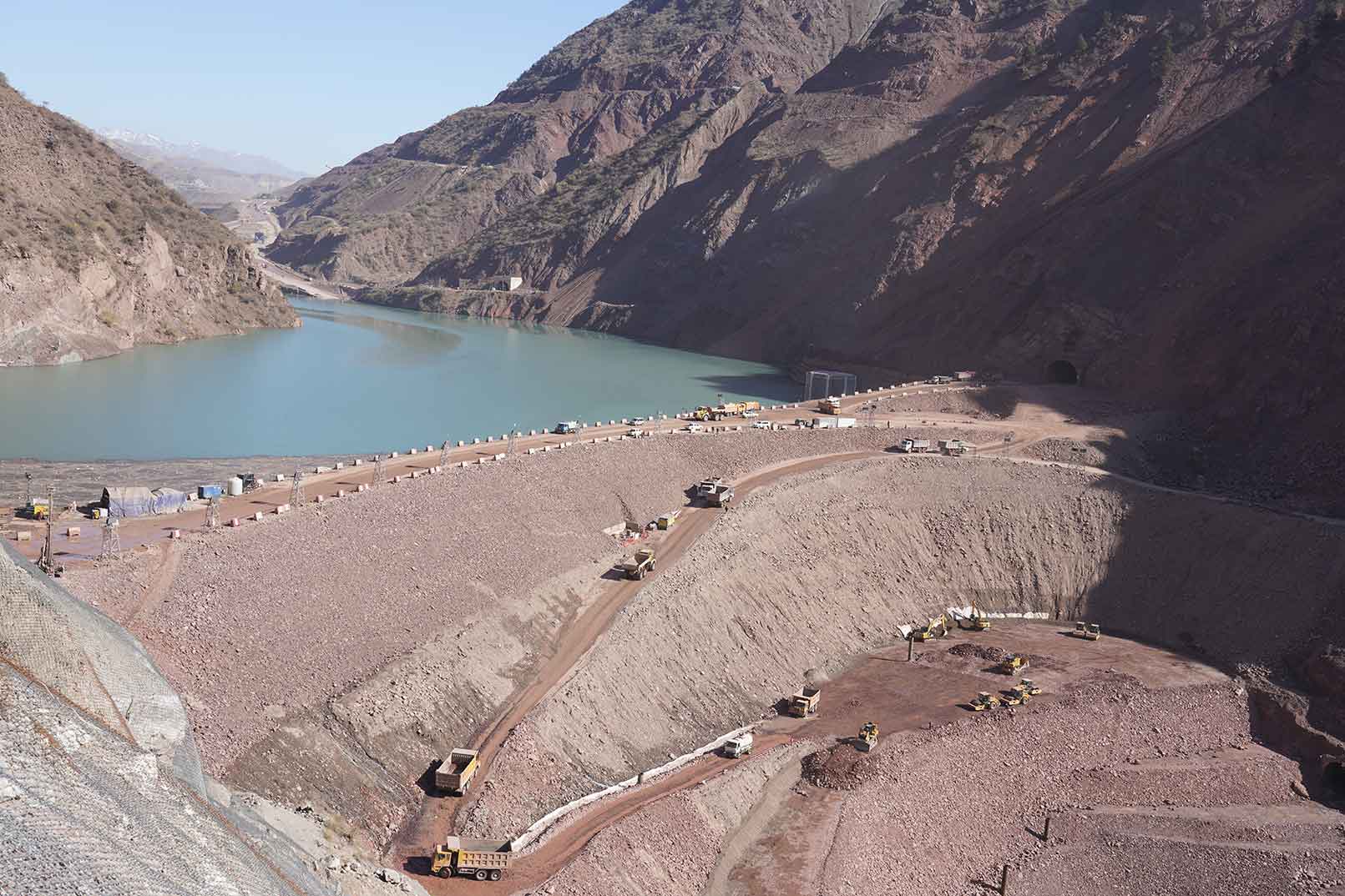Mountainous landscape with a large river or reservoir surrounded by steep rocky slopes and earthworks in progress.