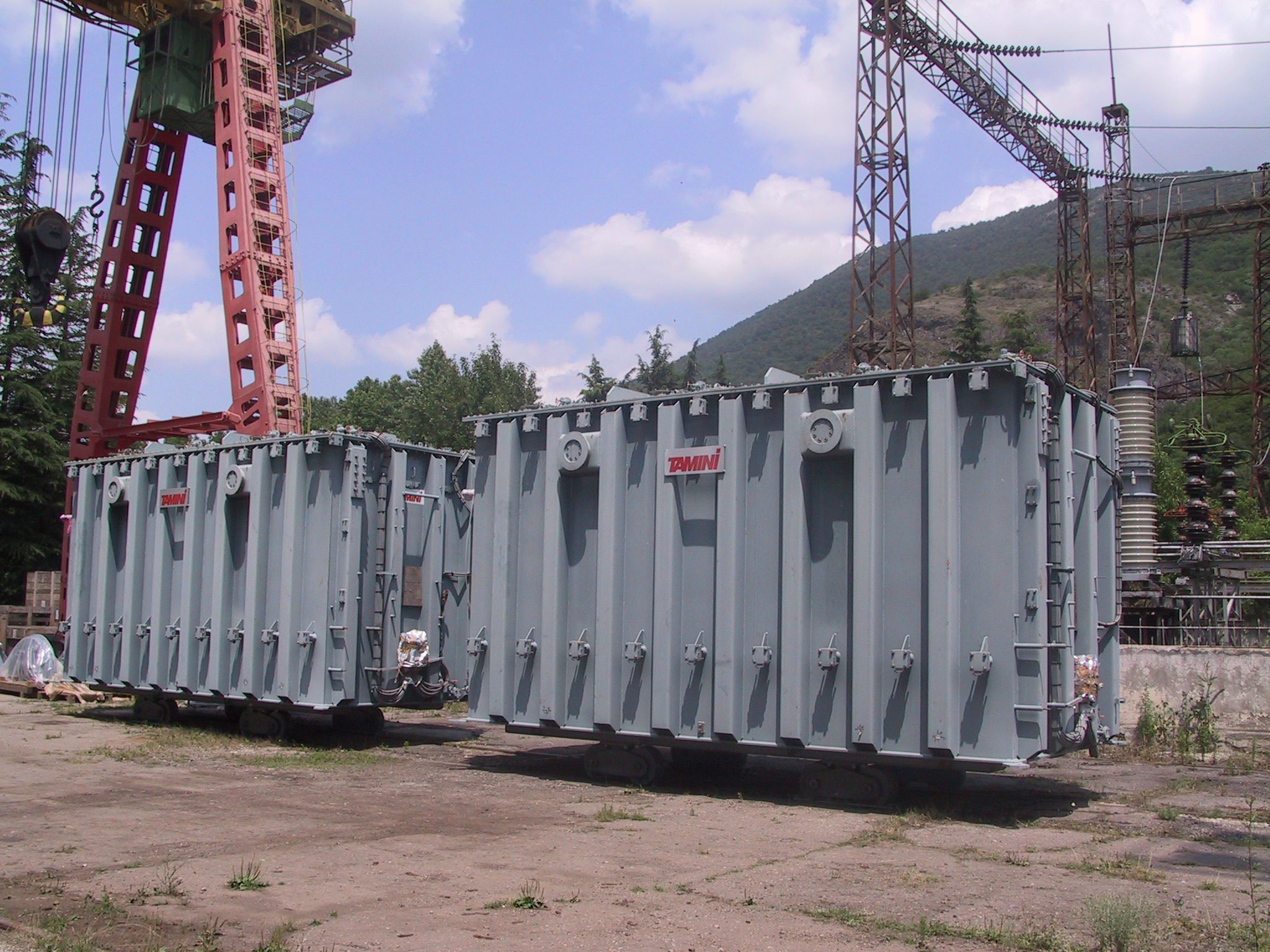 Large industrial transformers placed outdoors at an electrical substation site, surrounded by cranes and metal structures