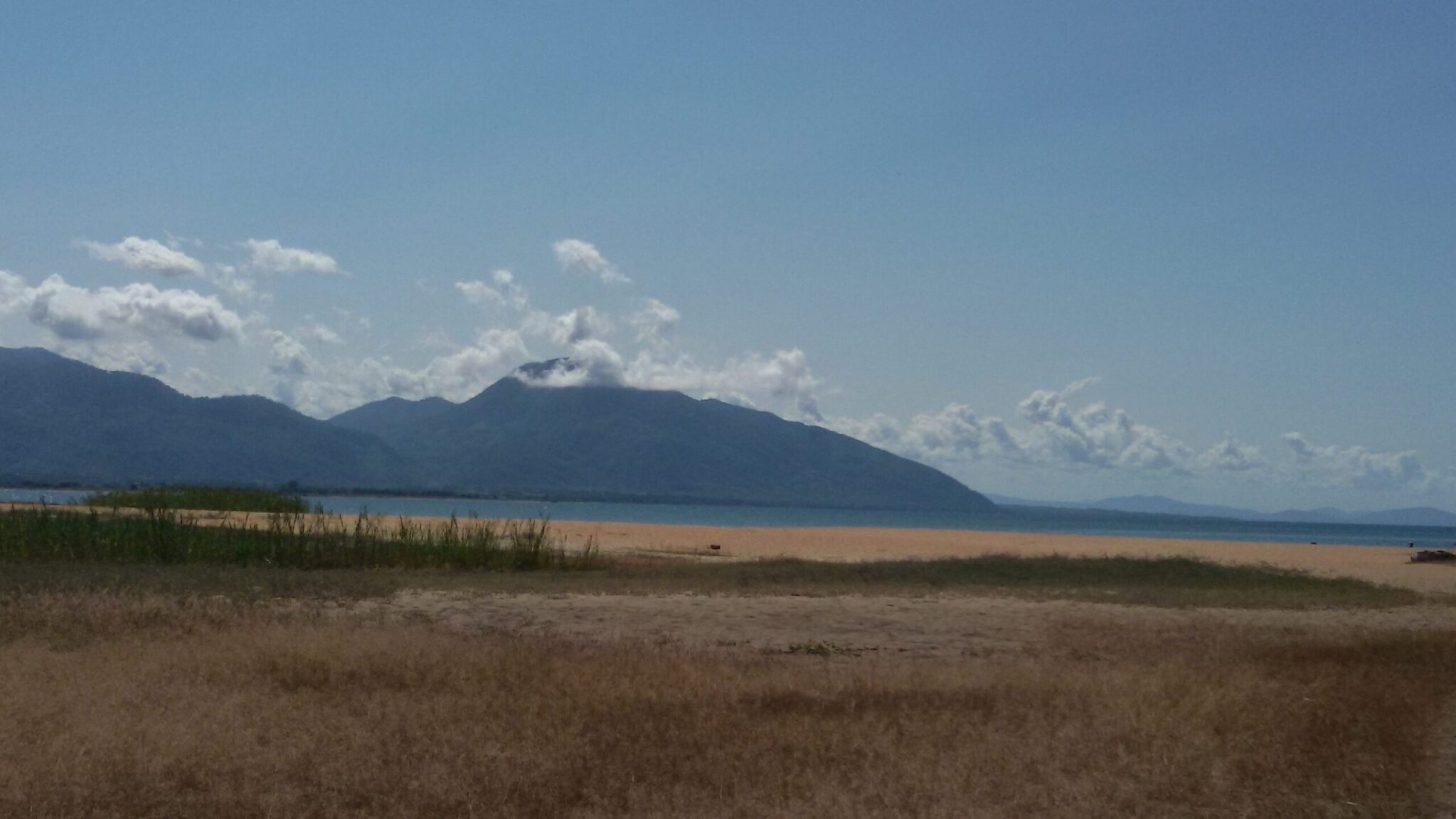 Scenic landscape with dry grassland in the foreground, a lake or body of water in the midground, and mountains under a clear blue sky in the background