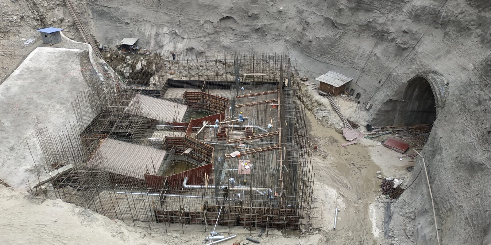 Construction site of an underground hydroelectric facility, with steel reinforcements and a tunnel entrance carved into the rock