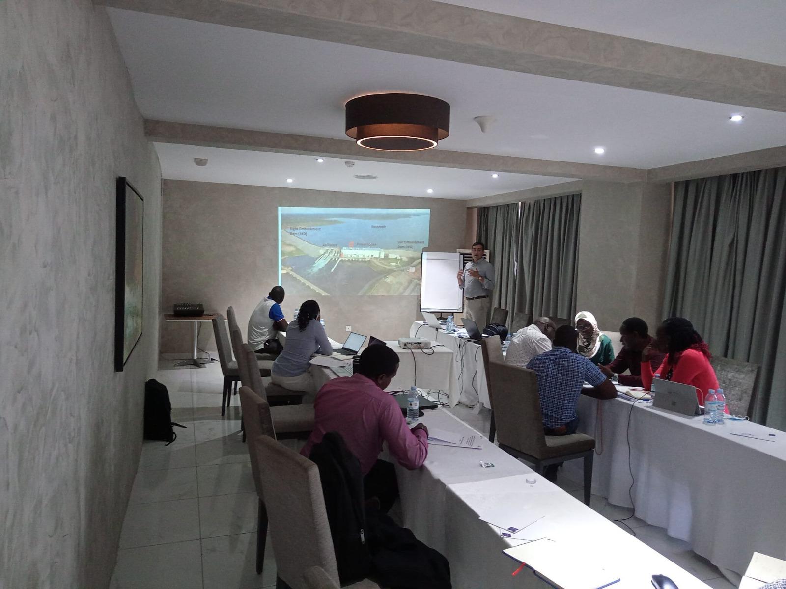 Training session or workshop in a conference room, with participants seated around tables and a presenter using a projector and flip chart