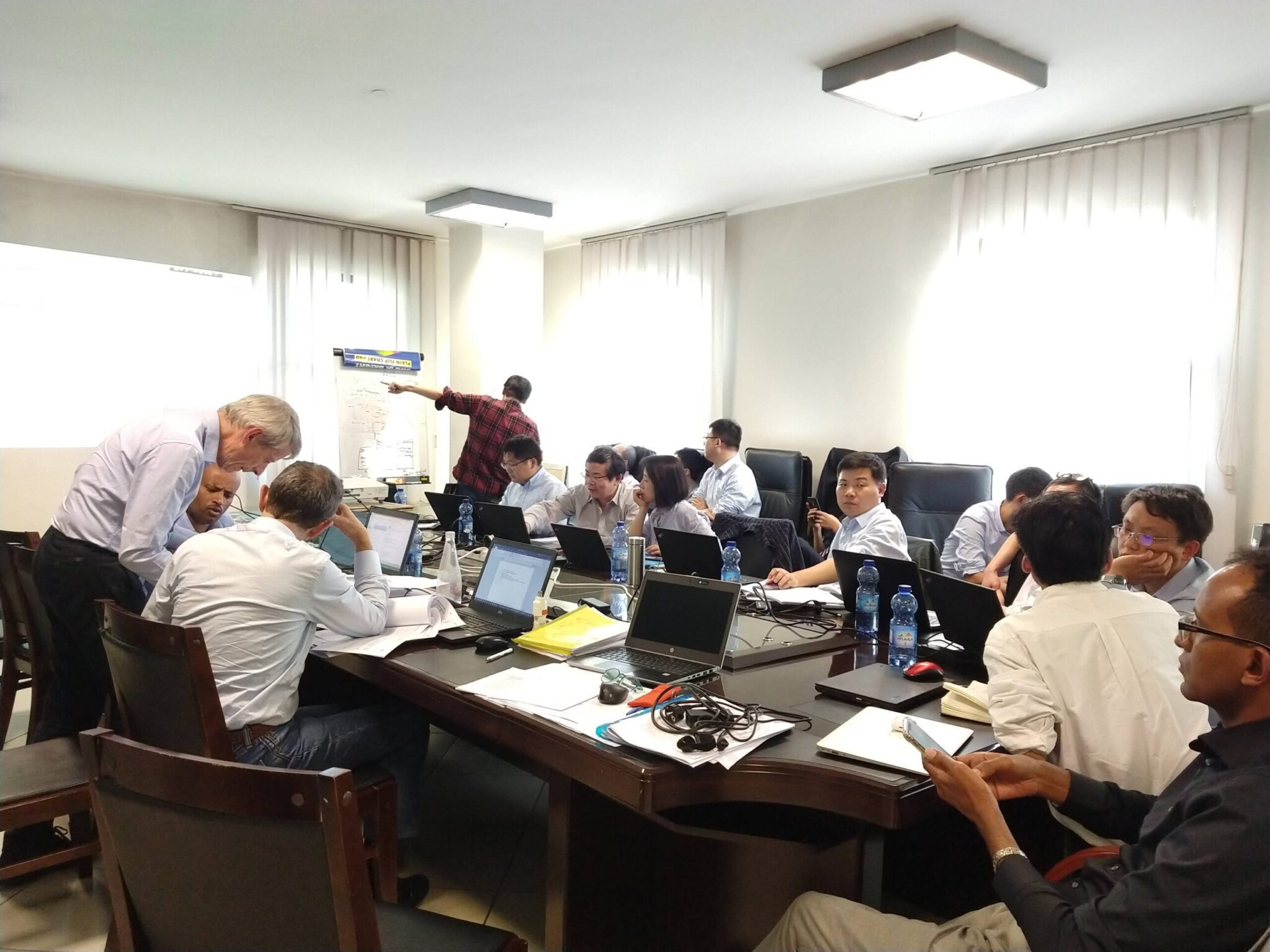 Group of professionals gathered around a conference table with laptops during a collaborative technical meeting or training session, with one person presenting