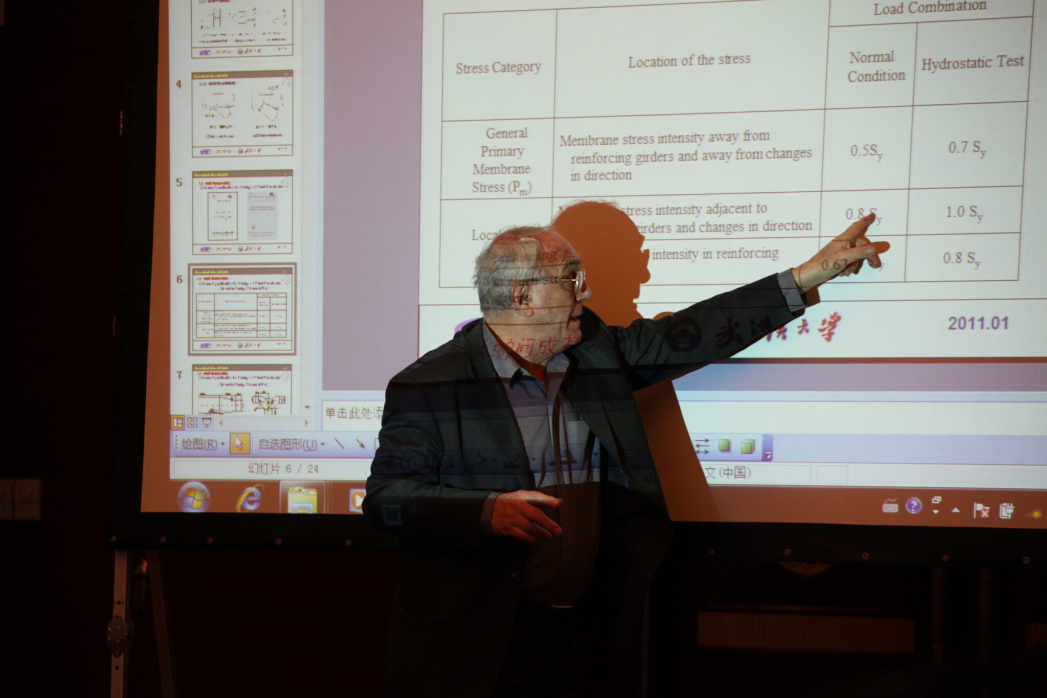 Man giving a presentation and pointing at a projected slide containing a table with data and text
