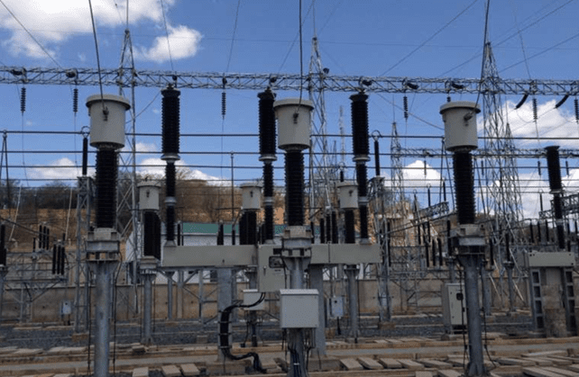 Close-up view of high-voltage equipment and insulators at an electrical substation, with multiple conductors and steel structures under a blue sky
