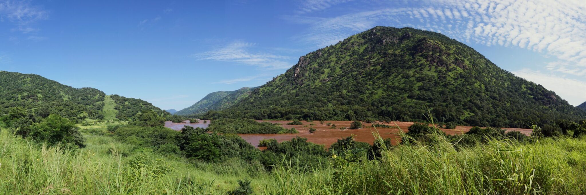 Panoramic view of a lush green mountainous landscape with a river or reservoir partially visible in the valley
