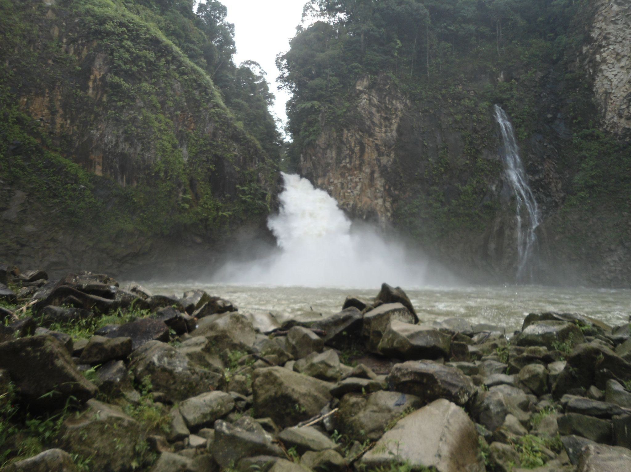 A Hydropower Project in featuring a concrete gravity dam. The natural landscape surrounding the waterfall highlights the mountainous terrain and lush vegetation.